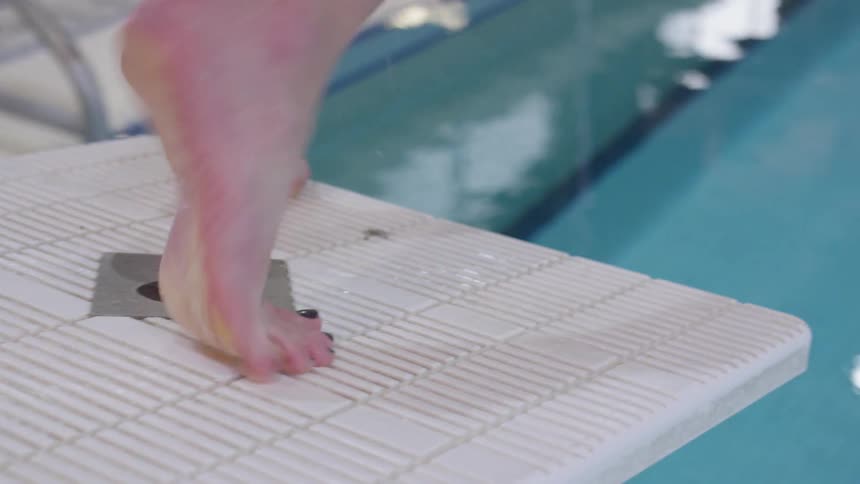 A female swimmer dives off a diving platform into an indoor swimming pool