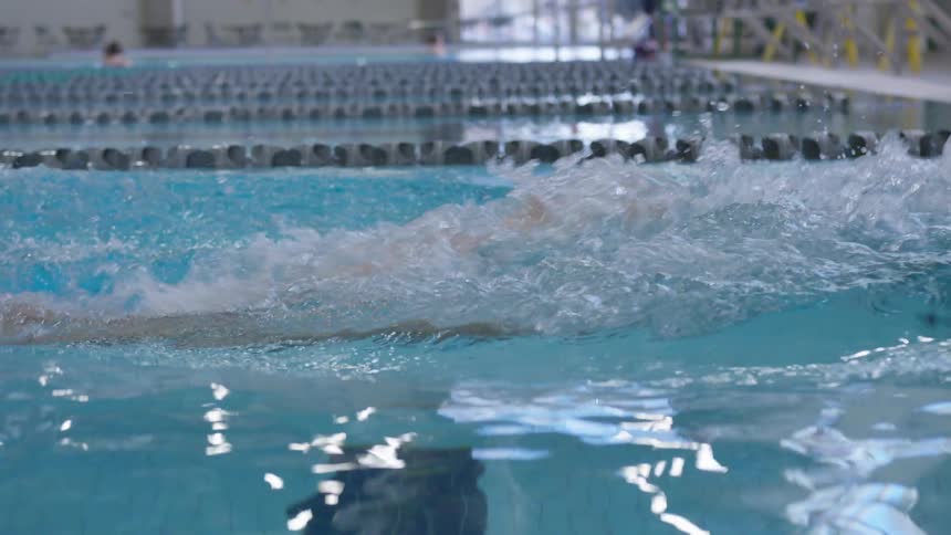 A woman wears a swim cap and goggles as she swims laps in an indoor pool