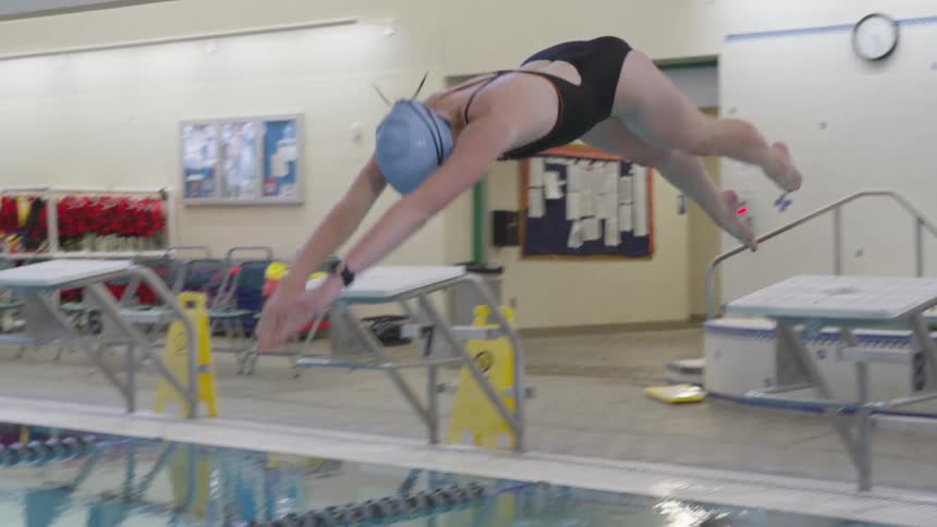 A woman dives off a diving board into an indoor swimming pool