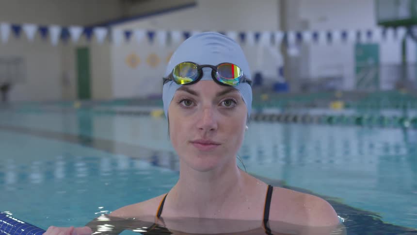 Woman in swim cap and goggles in olympic pool smiling