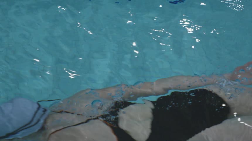 A female in a swimming cap and black bathing suit swims in a pool