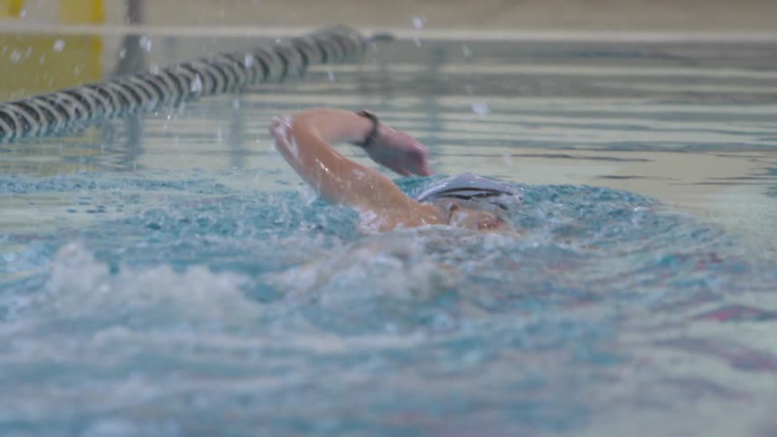 A woman free style swims quickly down a lane in a large indoor swimming pool