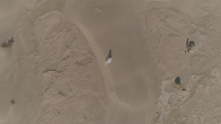 A woman walks through the sands of a desert as her clothing flutters behind her in the wind