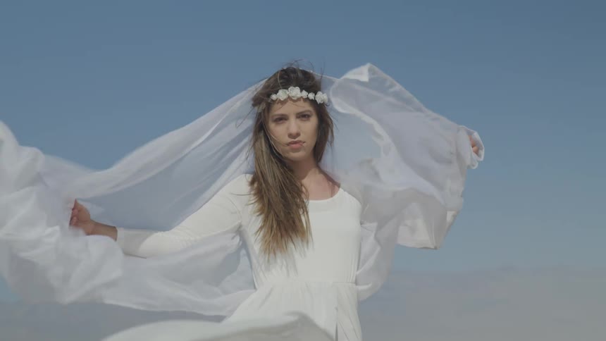A woman standing in the desert with a white dress blowing in the wind with the sky in the background