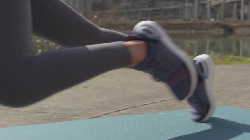 A female wearing gray leggings performs a leg exercise while outdoors