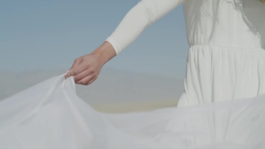 A woman is standing in the wind wearing a long white gown