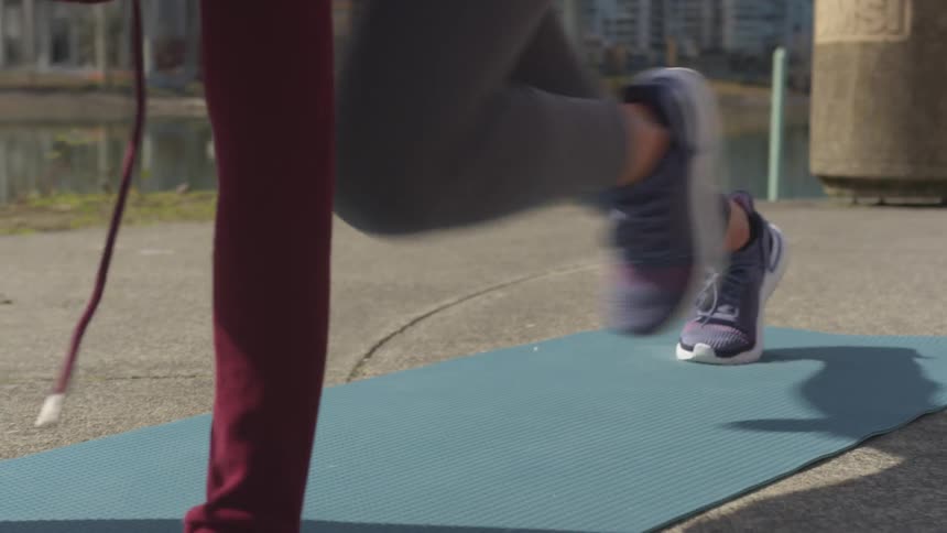 A young women exercises vigorously while outdoors atop a fitness mat