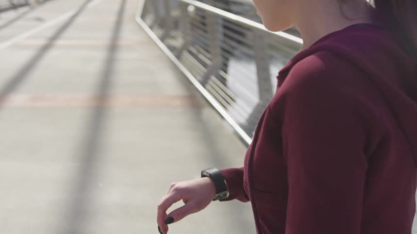 A white woman checks a wrist tracker before jogging across a bridge