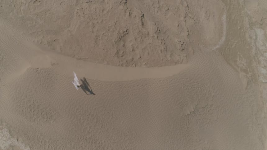 A woman walks through sand in a billowy white dress