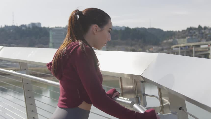 A teenage girl leans on a bridge and looks out at the water
