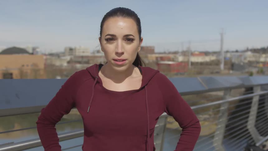 Young woman wearing sports clothes stands on a building next to a small city