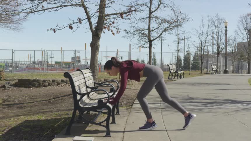 A woman steps on a park bench to stretch her legs for running