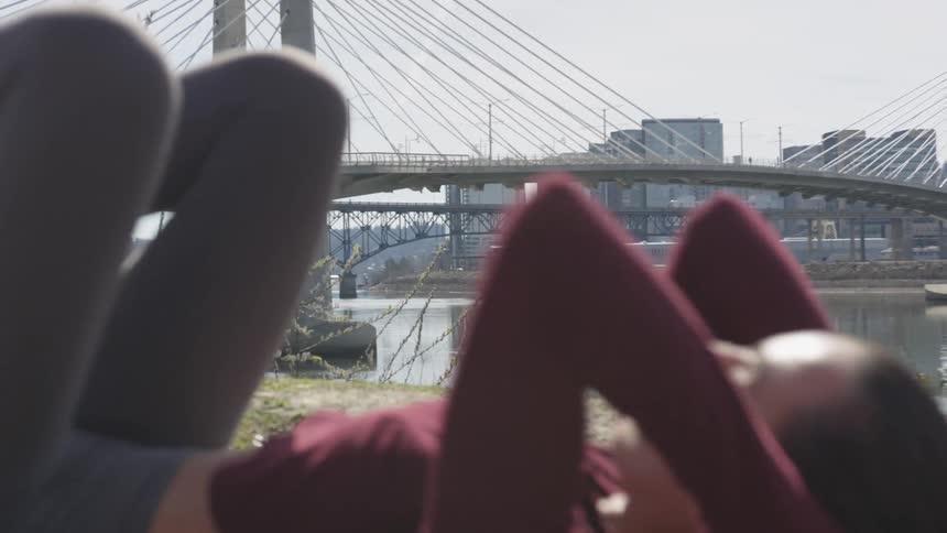 A teenage girl does sit ups in a public park with the city skyline in the distance