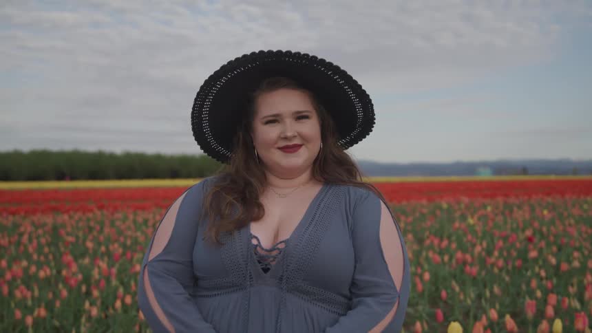 A woman standing in a field of colorful flowers slowly turns her head to smile into the camera