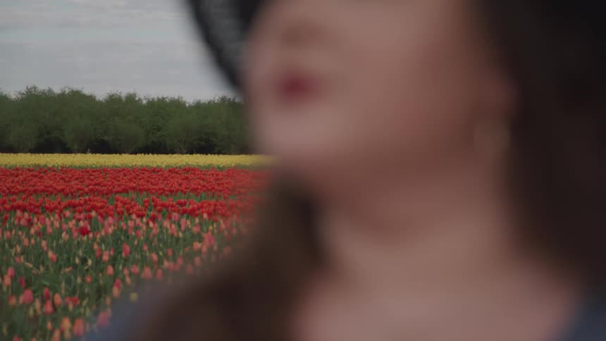 A woman stands in a field of colorful flowers on a cloudy day