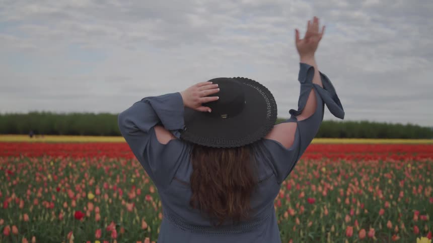 Young woman wearing a hat stands in front of a tulip field