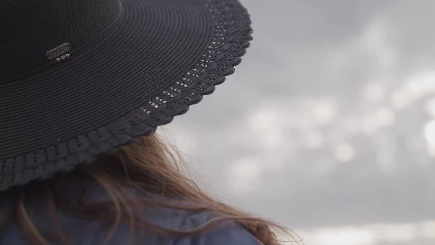 Back of the head of a woman with long hair wearing a hat outdoors