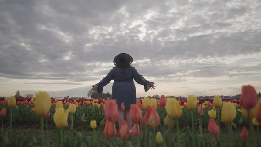 A woman stands in a field of flowers with her stretched out to her sides