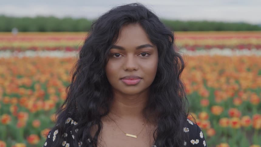 A young woman smiles into the camera while standing in a field of colorful flowers