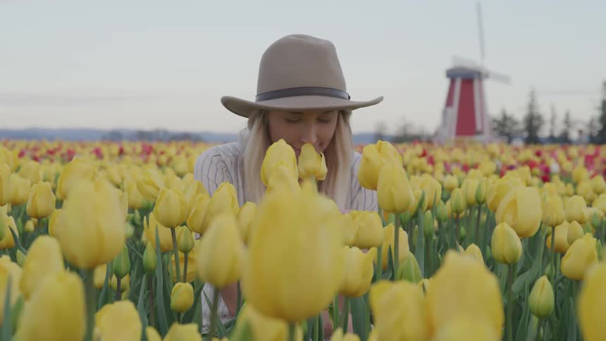 A woman kneeling in a field of colorful flowers holds one to her nose to smell its scent