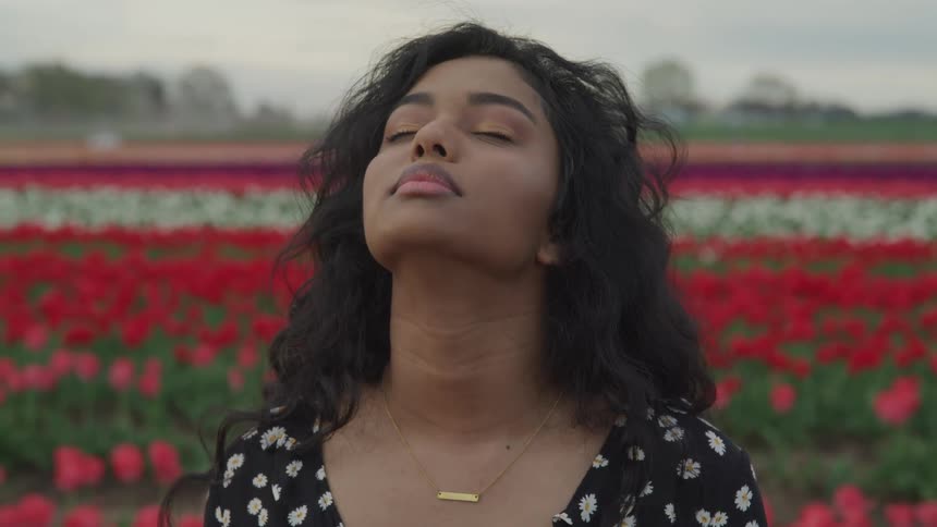 A teenage girl in a field of flowers with her eyes closed looking up towards the sky