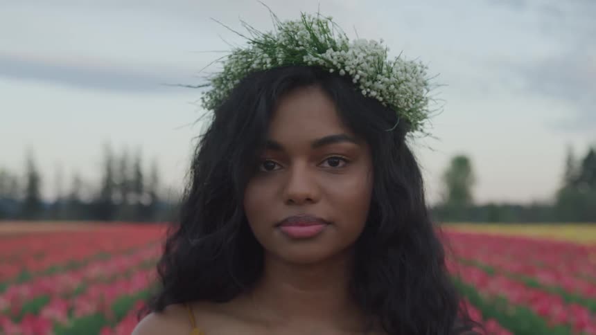 Young woman in flower crown standing in field with rows of flowers