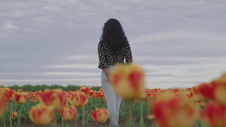 A woman looks out into the distance as she stands in a field of flowers under a cloudy sky