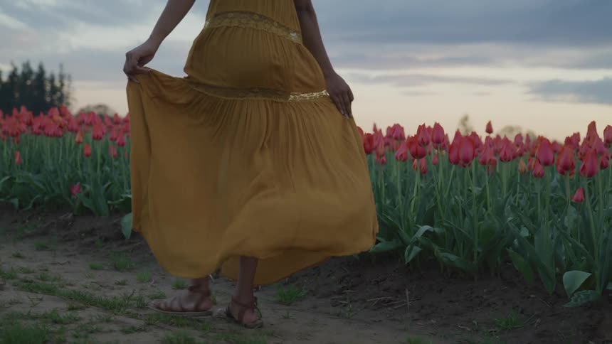 A woman in a long yellow dress skips and spins through a field of tulips