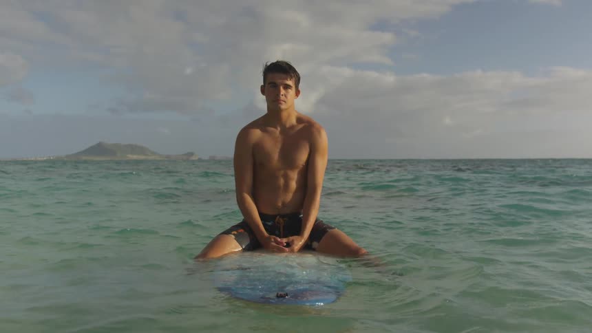 A surfer sits on a surfboard in the calm ocean on a cloudy day