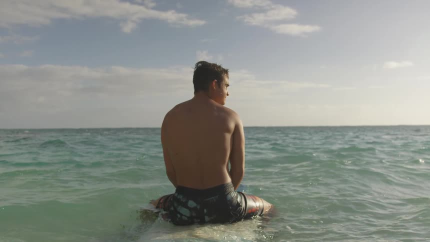 Man sits on board looking out across sea as waves ripple past