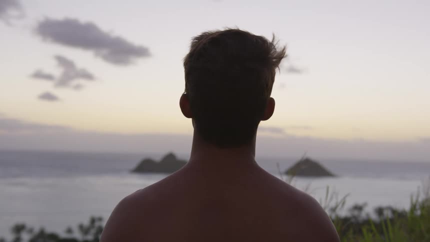 A man is standing outdoors at dusk by the beach