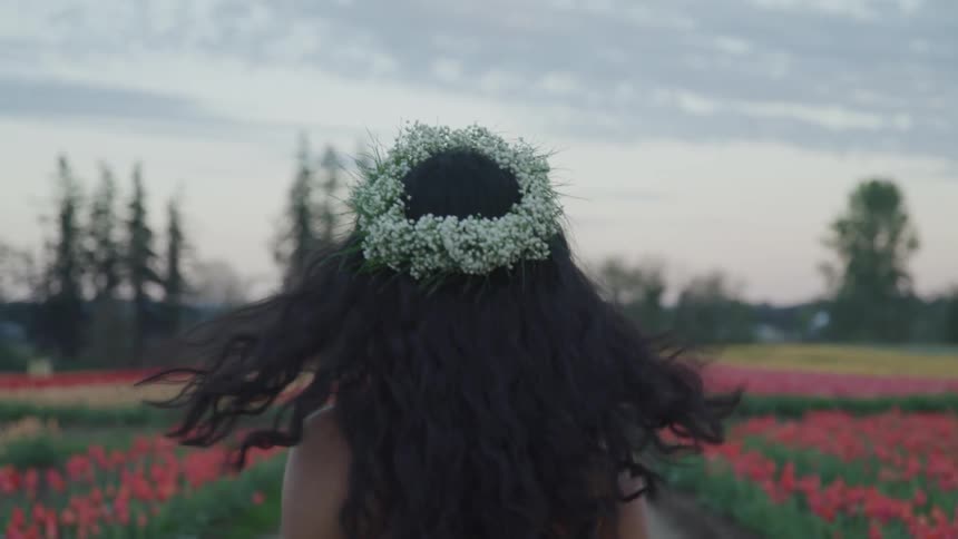 A woman walks through a field of flowers wearing a headdress