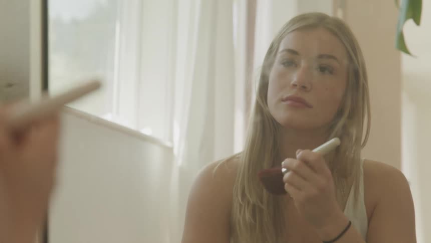 A woman putting makeup on her face in a mirror