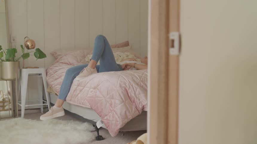 Woman with jeans and a white shirt lies on bed in bedroom