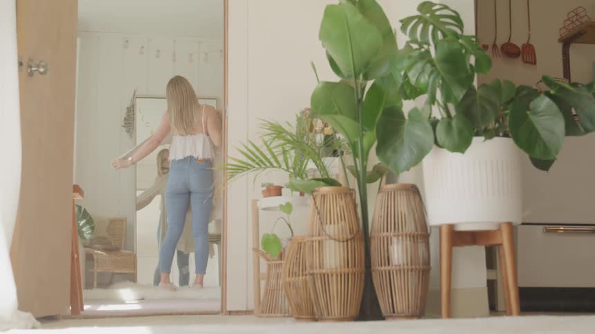 A woman holds a shirt up to her body while checking her appearance in a full length mirror