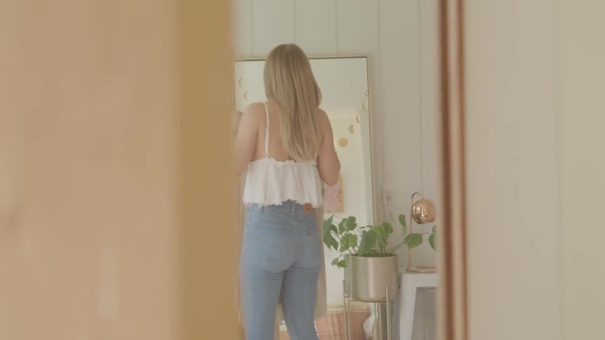 A woman standing in front of a mirror holding up a top on a hanger