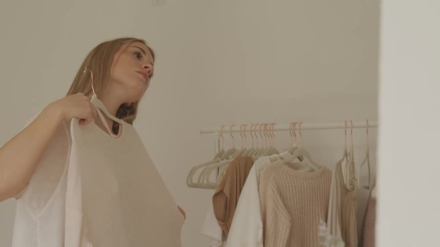 A teenage girl holds clothes up against her body and looks at them