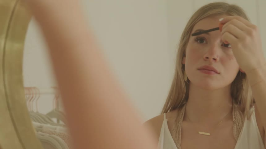 A woman is putting on makeup while looking in a mirror