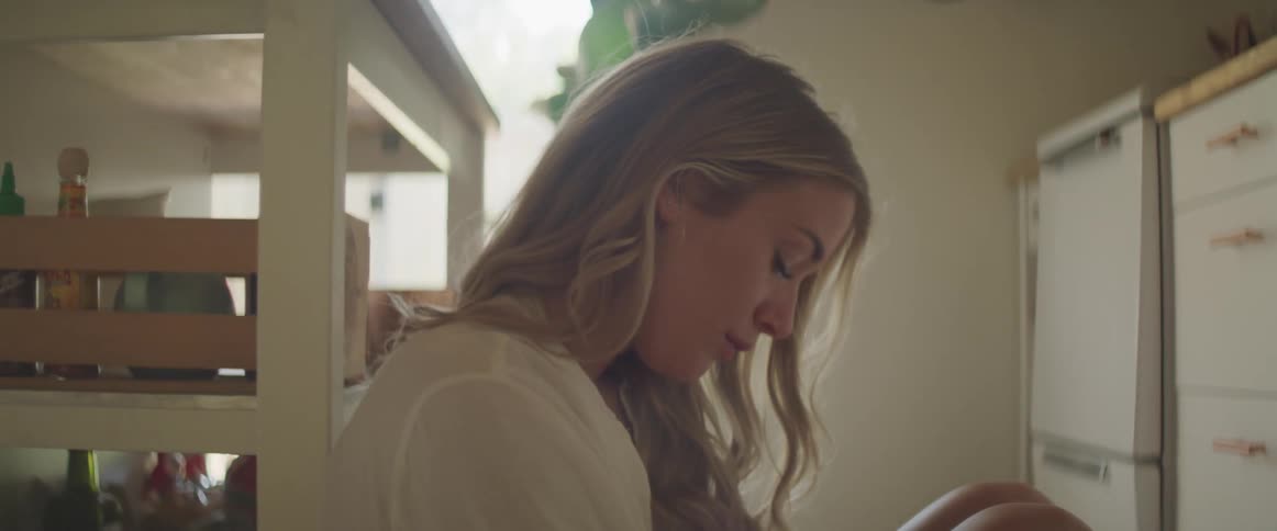 Blonde woman sits on kitchen floor leaning head back against furniture