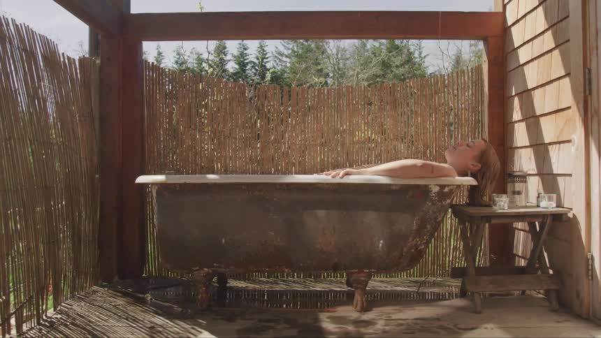 A woman laying down in a bathtub in a back porch next to a table