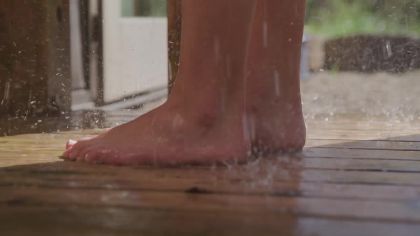 A persons feet as they shower near an open door leading outside