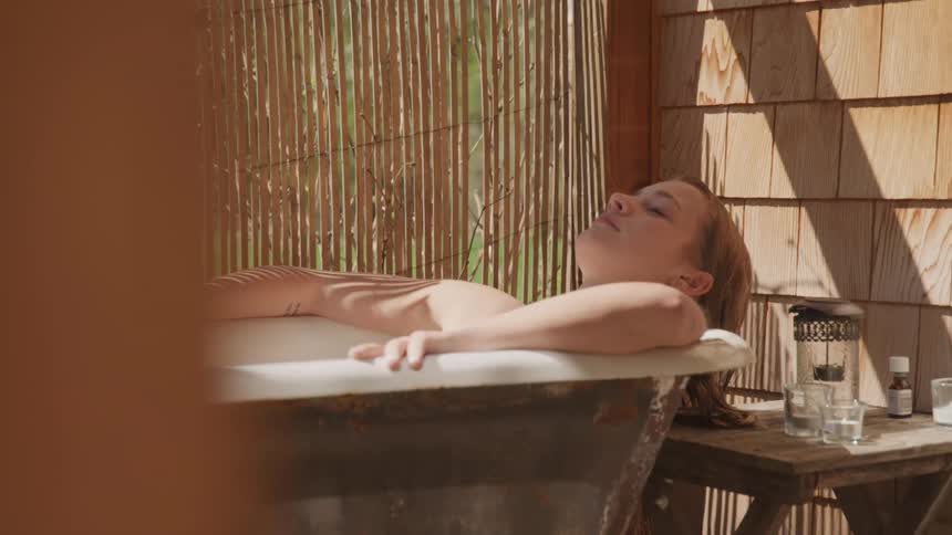 A female soaking in a bathtub in a hut outside