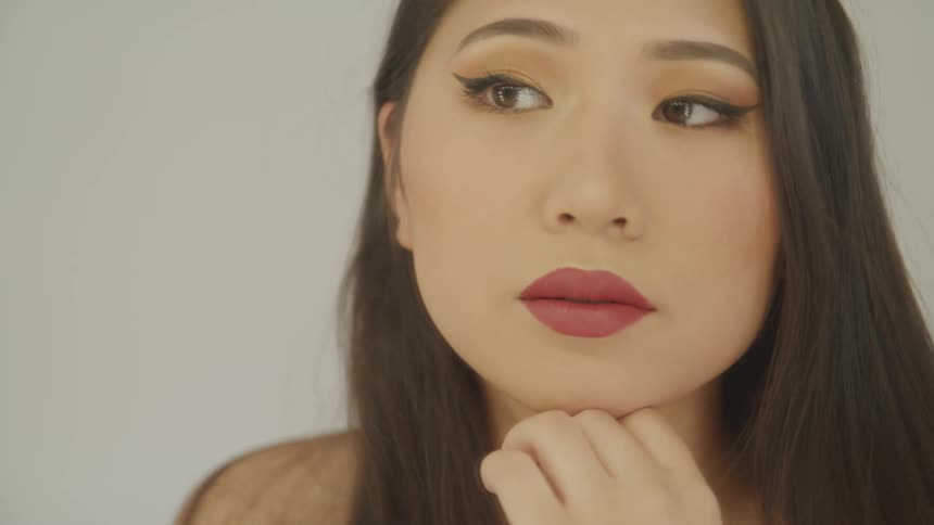 Asian woman with makeup and long hair looks in a mirror and smiles