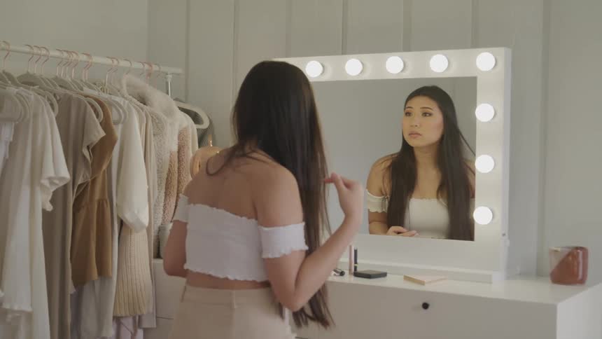 A woman standing next to clothing and fixing her hair in the mirror