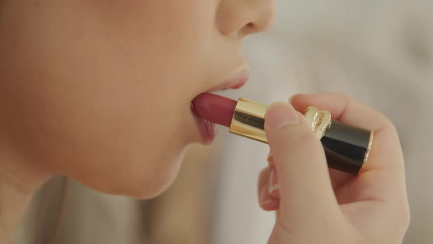 A woman is putting on lipstick