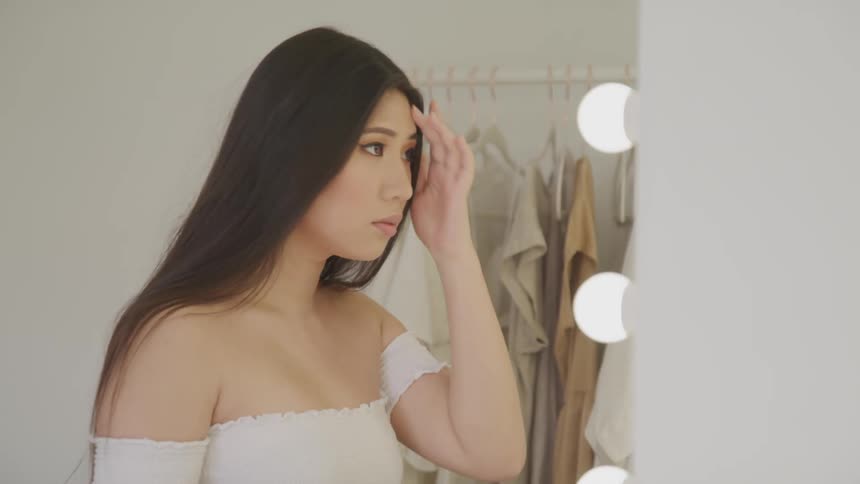 Young woman looks in mirror and fixes hair