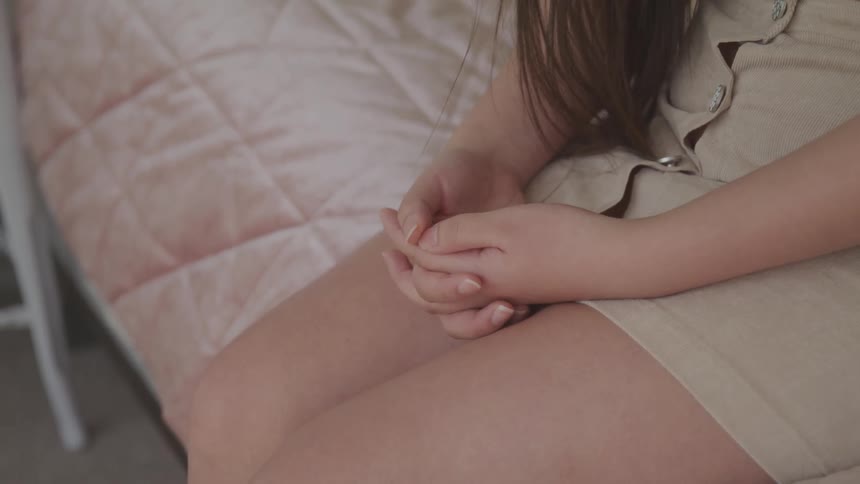 Young woman sitting in a bed with holding her hands over her lap