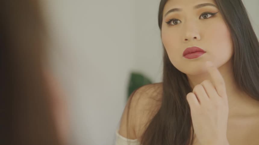 A woman examines her hair and made up face in the mirror