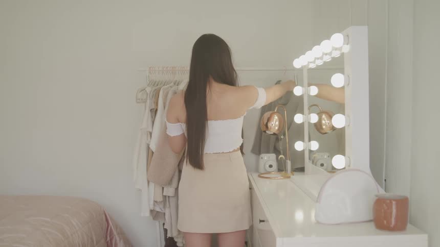 Young woman selecting clothing from rack in bedroom