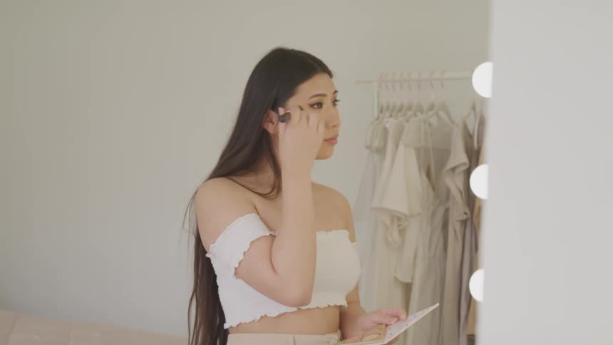 A teenage girl puts make up on in front of a lit up mirror